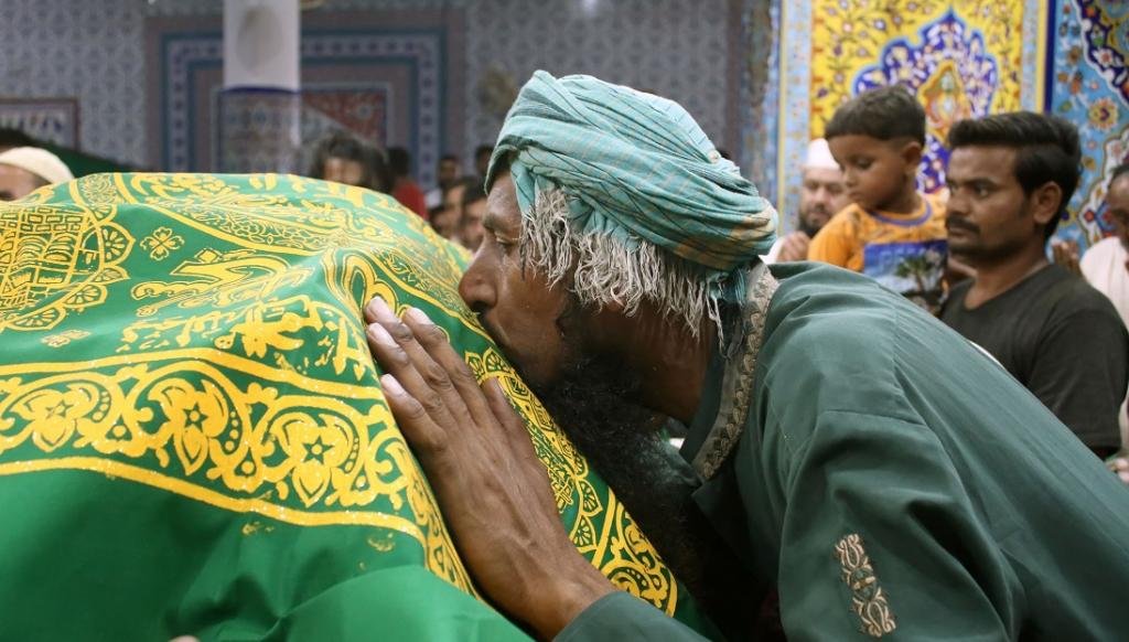 कराची में अब्दुल्ला शाह गाजी की दरगाह पर चादर को चूमती एक श्रद्धालु।  फोटो: आईस्टॉक